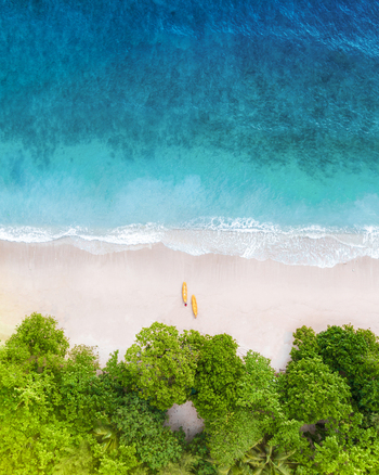 Aerial view of Pantai Gatra with two yellow kayaks resting on the white sand beach bordered by lush green trees and turquoise ocean waves in Malang Regency East Java Indonesia. Aerial view of Pantai Gatra with two yellow kayaks resting on the white sand beach bordered by lush green trees and turquoise ocean waves in Malang Regency East Java Indonesia.