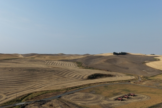 Aerial view of the rolling hills and harvested wheat fields of the Palouse region with farm equipment parked in the foreground under a clear sky in Palouse Washington United States. Aerial view of the rolling hills and harvested wheat fields of the Palouse region with farm equipment parked in the foreground under a clear sky in Palouse Washington United States.