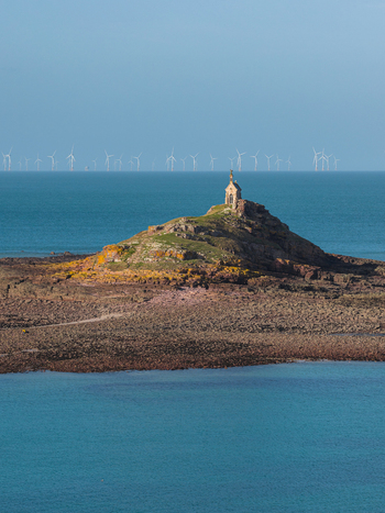 Aerial view of the Saint Michel chapel on a rocky islet with offshore wind turbines in the background and clear blue water Plurien Brittany France. Aerial view of the Saint Michel chapel on a rocky islet with offshore wind turbines in the background and clear blue water Plurien Brittany France.