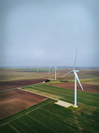 Aerial view of towering white wind turbines standing amidst a patchwork of green and brown fields under a soft overcast sky Châteaudun Centre Val de Loire France. Aerial view of towering white wind turbines standing amidst a patchwork of green and brown fields under a soft overcast sky Châteaudun Centre Val de Loire France.