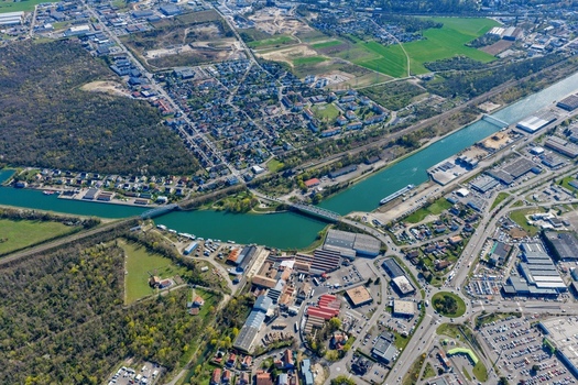 Aerial view of roads and tree lines meet the waterway the green fields contrast with the urban sprawl Sausheim Grand Est France.