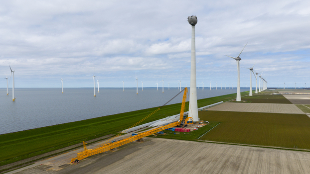 Aerial view of a large yellow crane performing maintenance on a wind turbine tower with rows of turbines in the water and agricultural fields in Espel Flevoland Netherlands. Aerial view of a large yellow crane performing maintenance on a wind turbine tower with rows of turbines in the water and agricultural fields in Espel Flevoland Netherlands.