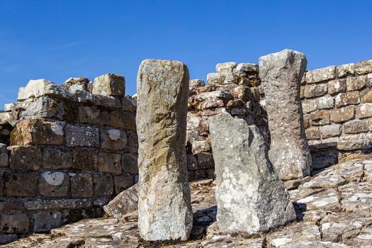 View of the ancient stone pillars and weathered masonry walls at the Vindolanda Roman fort archaeological site under a clear blue sky Hexham England United Kingdom. View of the ancient stone pillars and weathered masonry walls at the Vindolanda Roman fort archaeological site under a clear blue sky Hexham England United Kingdom.