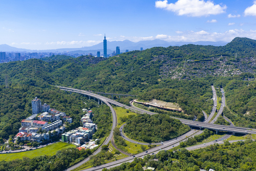 Aerial view of the Taipei 101 skyscraper rising above the lush green hills and a complex highway interchange in the urban landscape of Taipei Taipei City Taiwan. Aerial view of the Taipei 101 skyscraper rising above the lush green hills and a complex highway interchange in the urban landscape of Taipei Taipei City Taiwan.