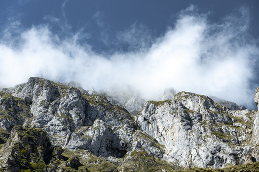 View of craggy gray mountains rise their peaks shrouded in ethereal white clouds against a backdrop of deep blue sky Picos de Europa Asturias Spain. View of craggy gray mountains rise their peaks shrouded in ethereal white clouds against a backdrop of deep blue sky Picos de Europa Asturias Spain.