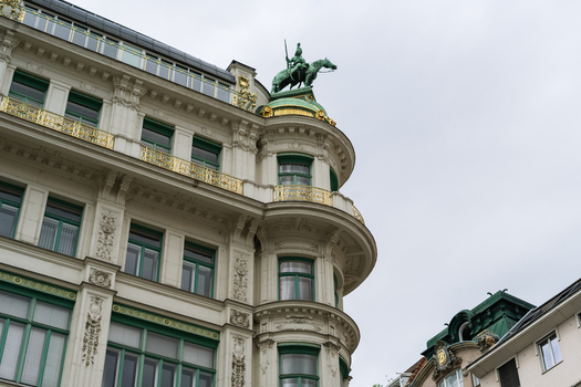 View of the ornate facade of a historic building featuring golden balconies and an equestrian statue on a green dome in Vienna Vienna Austria. View of the ornate facade of a historic building featuring golden balconies and an equestrian statue on a green dome in Vienna Vienna Austria.