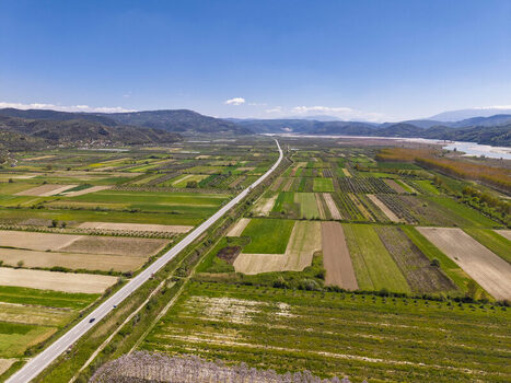 Aerial view of agricultural fields a long straight road cutting through the landscape and distant mountains under a clear blue sky in Lushnje Fier County Albania. Aerial view of agricultural fields a long straight road cutting through the landscape and distant mountains under a clear blue sky in Lushnje Fier County Albania.
