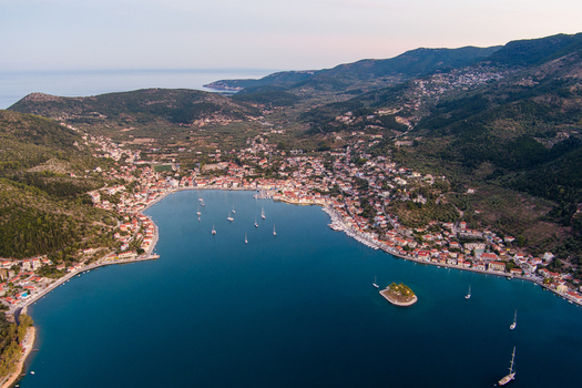 Aerial view of the town of Vathy on Ithaca island featuring a deep blue bay with sailboats surrounded by lush green hills and Mediterranean architecture in Ithaki Greece.