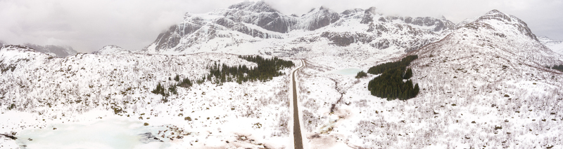 Aerial view of the snow covered landscape of Lofoten with a road winding through the mountains evergreen trees and frozen ponds in Nordland Norway.