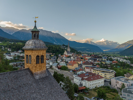 Aerial view of St. Laurentius Church with its wooden shingled tower overlooking the historic town of Imst nestled in the Austrian Alps during golden hour in Imst Tyrol Austria.