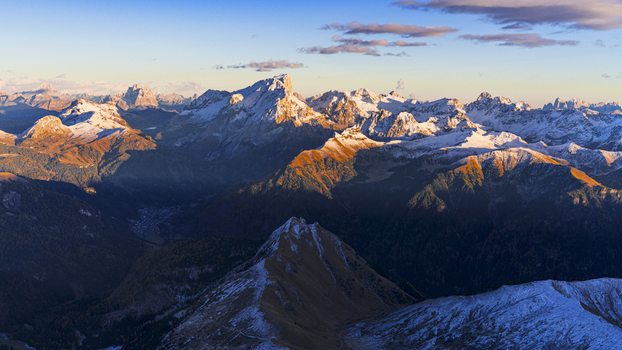 Aerial view of sunlit snow capped peaks and shadowed valleys create a dramatic tapestry of light and dark across the mountainous landscape Dolomites Italy.