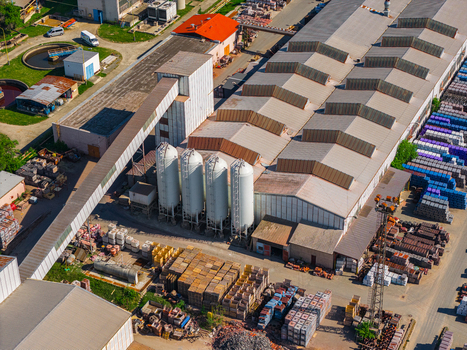 Aerial view of an industrial facility with white storage silos a long conveyor bridge and outdoor storage areas with stacked materials in Kyjov South Moravian Region Czechia.