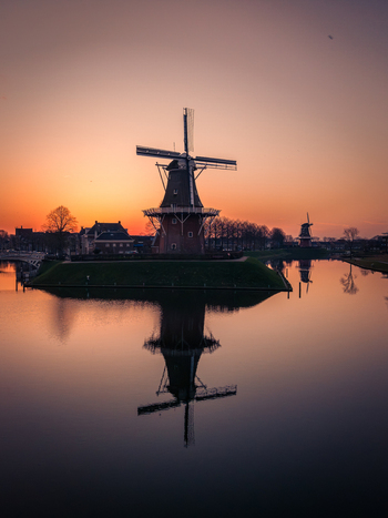 Aerial view of a traditional Dutch windmill reflected in the calm water of a canal during a vibrant sunset in Dokkum Friesland Netherlands. Aerial view of a traditional Dutch windmill reflected in the calm water of a canal during a vibrant sunset in Dokkum Friesland Netherlands.
