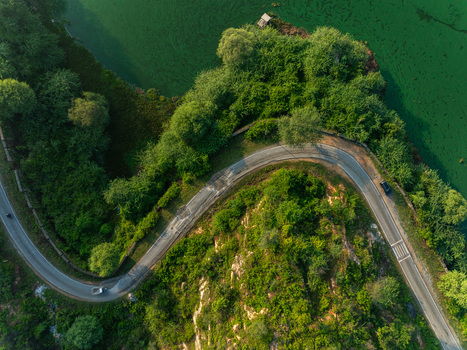 Aerial view of a winding road along the lush green banks of a lake with rocky terrain in Udaipur Rajasthan India. Aerial view of a winding road along the lush green banks of a lake with rocky terrain in Udaipur Rajasthan India.
