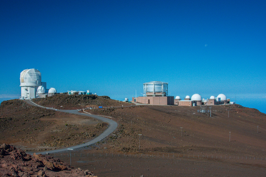 View of the Haleakala Observatory with its large telescope domes situated on the volcanic landscape of Maui under a clear blue sky Maui County Hawaii United States.