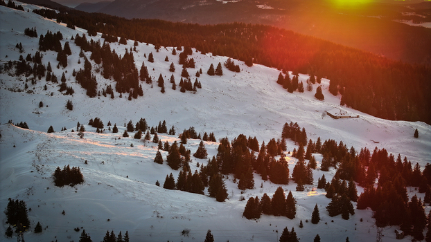 Aerial view of Col de la Faucille mountain pass covered in snow with pine trees and a small chalet during sunset in Gex Auvergne Rhone Alpes France. Aerial view of Col de la Faucille mountain pass covered in snow with pine trees and a small chalet during sunset in Gex Auvergne Rhone Alpes France.