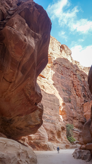 View of a person walking through the narrow Siq canyon with towering red sandstone cliffs under a bright blue sky in Wadi Musa Ma an Governorate Jordan. View of a person walking through the narrow Siq canyon with towering red sandstone cliffs under a bright blue sky in Wadi Musa Ma an Governorate Jordan.