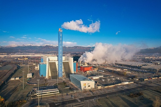 Aerial view of the TRM Iren waste to energy plant featuring a tall blue chimney with white smoke against the snow capped Alps in Torino Piemonte Italy. Aerial view of the TRM Iren waste to energy plant featuring a tall blue chimney with white smoke against the snow capped Alps in Torino Piemonte Italy.
