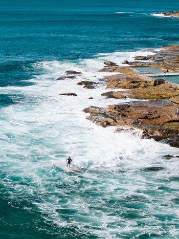 Aerial view of a surfer riding a wave near the rocky coastline and the Dee Why Rockpool in Dee Why New South Wales Australia. Aerial view of a surfer riding a wave near the rocky coastline and the Dee Why Rockpool in Dee Why New South Wales Australia.