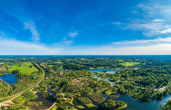 Aerial view of lush green forests winding lakes and open fields under a vast blue sky in Latvia. Aerial view of lush green forests winding lakes and open fields under a vast blue sky in Latvia.