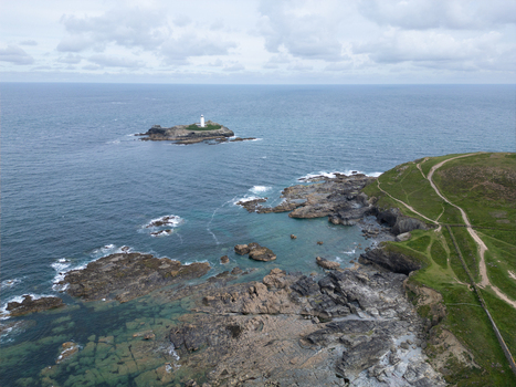 Aerial view of Godrevy Lighthouse on a rocky island surrounded by the blue sea and rugged cliffs of the coastline under a cloudy sky in Gwithian England United Kingdom. Aerial view of Godrevy Lighthouse on a rocky island surrounded by the blue sea and rugged cliffs of the coastline under a cloudy sky in Gwithian England United Kingdom.