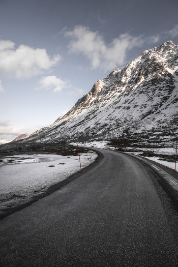 View of a winding asphalt road leading through snow covered mountains under a blue sky with soft clouds Kvaloya Troms Norway. View of a winding asphalt road leading through snow covered mountains under a blue sky with soft clouds Kvaloya Troms Norway.