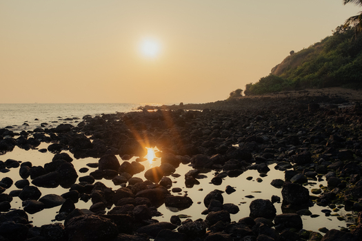 View of the sun s golden embrace kisses the dark rocky shore reflecting in tranquil tide pools as verdant hills rise Chiplun Maharashtra India. View of the sun s golden embrace kisses the dark rocky shore reflecting in tranquil tide pools as verdant hills rise Chiplun Maharashtra India.