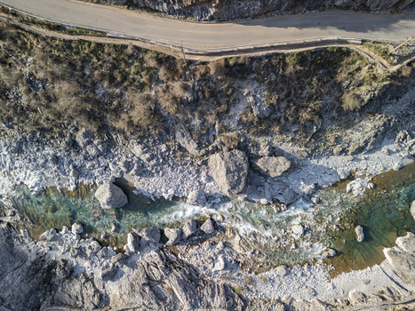 Aerial view of the rocky bed of the Kiri River with turquoise water flowing through rugged terrain and a winding road nearby in Shkoder Qarku i Shkodres Albania. Aerial view of the rocky bed of the Kiri River with turquoise water flowing through rugged terrain and a winding road nearby in Shkoder Qarku i Shkodres Albania.