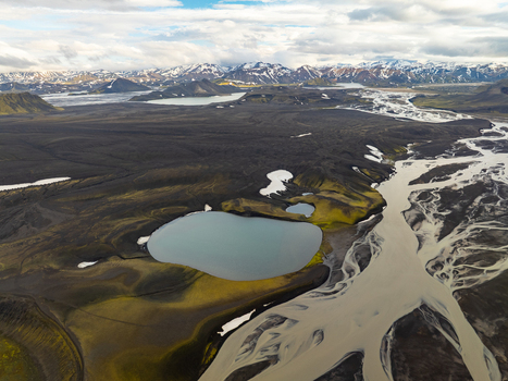 Aerial view of Landmannalaugar featuring dramatic volcanic terrain winding glacial rivers vibrant green mossy hills and snow capped mountains in Rangarthing ytra Iceland. Aerial view of Landmannalaugar featuring dramatic volcanic terrain winding glacial rivers vibrant green mossy hills and snow capped mountains in Rangarthing ytra Iceland.