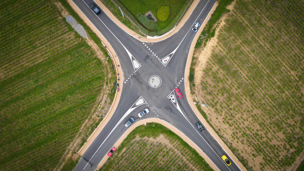 Aerial view of a rural road intersection with cars driving through green vineyards and agricultural fields La Chapelle de Guinchay Bourgogne Franche Comte France.