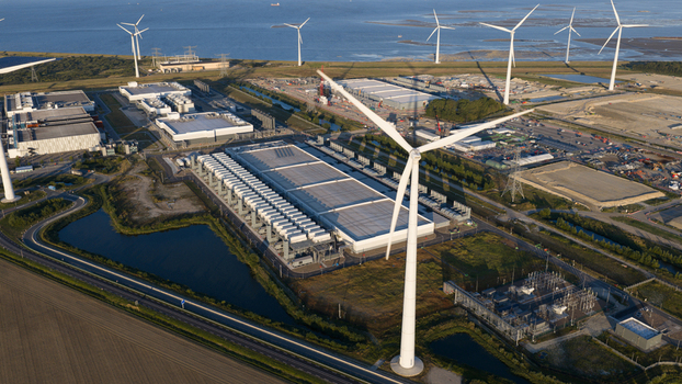Aerial view of a large data center facility surrounded by wind turbines green fields and coastal infrastructure in Eemshaven Groningen Netherlands.