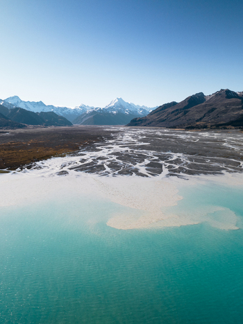 Aerial view of turquoise waters meet rugged snow capped mountains under a clear sky creating a stunning contrast of colors and textures Lake Tekapo Canterbury Region New Zealand. Aerial view of turquoise waters meet rugged snow capped mountains under a clear sky creating a stunning contrast of colors and textures Lake Tekapo Canterbury Region New Zealand.
