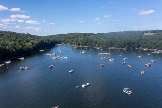 Aerial view of Lake Wallenpaupack with numerous boats scattered across the water surrounded by lush green forests under a clear blue sky in Tannersville Pennsylvania United States. Aerial view of Lake Wallenpaupack with numerous boats scattered across the water surrounded by lush green forests under a clear blue sky in Tannersville Pennsylvania United States.