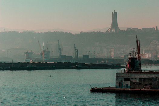 View of the Maqam Echahid monument overlooking the industrial port with cargo ships and cranes in Algiers Algeria.