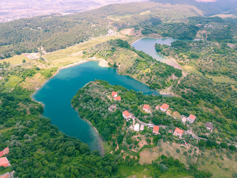 Aerial view of a turquoise lake winding through lush green hills with scattered houses featuring red rooftops Kruje Durres County Albania.