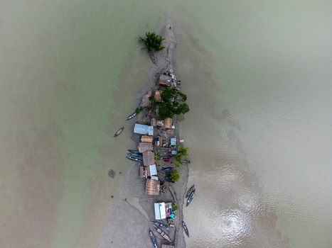 Aerial view of Kalabagi village on a narrow sandbar with small huts wooden boats and green trees surrounded by murky river water Khulna District Khulna Division Bangladesh.