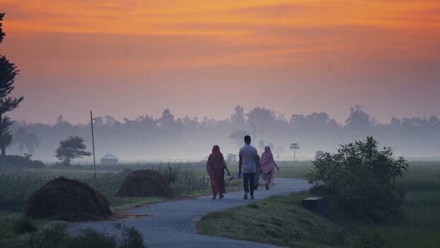 View of people walking on a rural road during a misty sunrise Bangladesh.