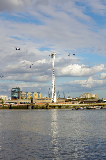 View of the IFS Cloud Cable Car crossing the River Thames with its distinctive white pylon and cabins against a cloudy sky in Greenwich London England United Kingdom. View of the IFS Cloud Cable Car crossing the River Thames with its distinctive white pylon and cabins against a cloudy sky in Greenwich London England United Kingdom.