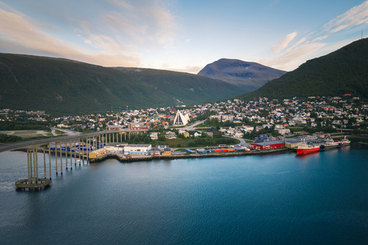 Aerial view of the Arctic Cathedral in Tromso featuring its iconic triangular architecture the Tromso Bridge colorful houses and the calm bay waters in Tromso Troms Norway. Aerial view of the Arctic Cathedral in Tromso featuring its iconic triangular architecture the Tromso Bridge colorful houses and the calm bay waters in Tromso Troms Norway.