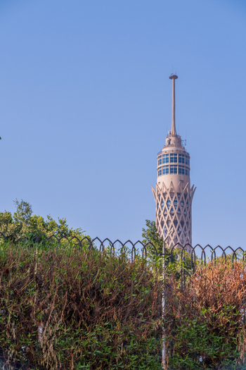 View of the iconic latticed Cairo Tower piercing the clear blue sky framed by vibrant greenery and a wrought iron fence Zamalek Cairo Governorate Egypt. View of the iconic latticed Cairo Tower piercing the clear blue sky framed by vibrant greenery and a wrought iron fence Zamalek Cairo Governorate Egypt.