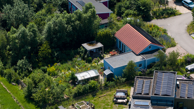 Aerial view of Ecodorp Bolderburen featuring sustainable houses with solar panels lush gardens and greenhouses surrounded by dense greenery in Almere Flevoland Netherlands. Aerial view of Ecodorp Bolderburen featuring sustainable houses with solar panels lush gardens and greenhouses surrounded by dense greenery in Almere Flevoland Netherlands.