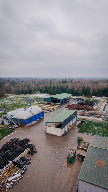 Valmiera Latvija 21 November 2025 Aerial view of a waste management and recycling facility with industrial buildings piles of tires and compost areas surrounded by forest.