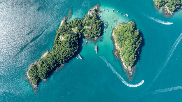 Aerial view of Lagoa Azul also known as the Blue Lagoon featuring lush green islands surrounded by turquoise waters with boats and boat wakes in Angra dos Reis Rio de Janeiro Brazil.