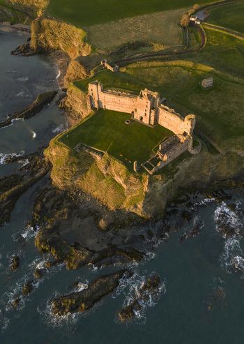 Aerial view of Tantallon Castle perched on a steep cliff overlooking the North Sea with golden sunlight hitting the ancient stone walls North Berwick Scotland United Kingdom.