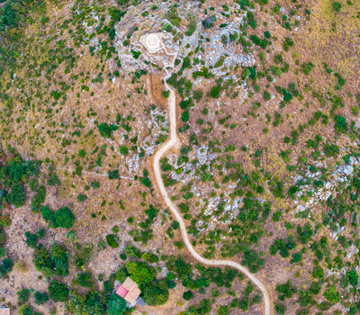 Aerial view of a winding dirt path leading to a small stone structure atop a rocky hill surrounded by Mediterranean vegetation in Palermo Sicily Italy. Aerial view of a winding dirt path leading to a small stone structure atop a rocky hill surrounded by Mediterranean vegetation in Palermo Sicily Italy.