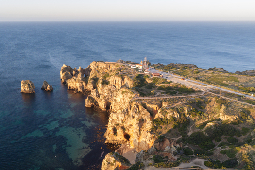 Aerial view of the iconic Ponta da Piedade lighthouse perched on dramatic golden cliffs overlooking the turquoise Atlantic Ocean in Lagos Faro District Portugal.