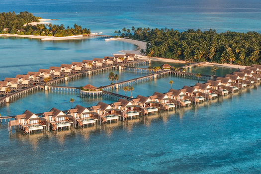 Aerial view of overwater bungalows connected by wooden walkways over a turquoise lagoon surrounded by lush tropical vegetation on a small island near Kudahuvadhoo Dhaalu Atoll Maldives. Aerial view of overwater bungalows connected by wooden walkways over a turquoise lagoon surrounded by lush tropical vegetation on a small island near Kudahuvadhoo Dhaalu Atoll Maldives.