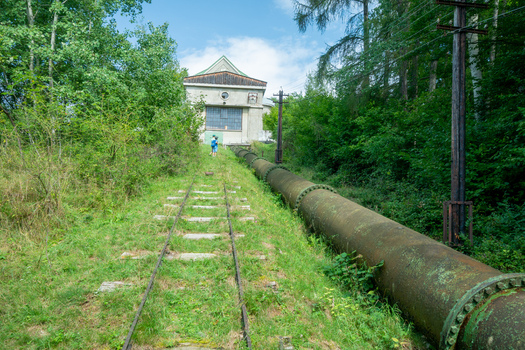 View of Jasenie Hydroelectric Power Plant with its large metal penstock pipe and railway tracks leading to the building set in forest in Jasenie Banska Bystrica Regio Slovakia.