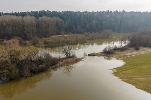 Aerial view of a flooded river overflowing into green agricultural fields and leafless trees under an overcast sky Kaniukai Kaunas County Lithuania. Aerial view of a flooded river overflowing into green agricultural fields and leafless trees under an overcast sky Kaniukai Kaunas County Lithuania.