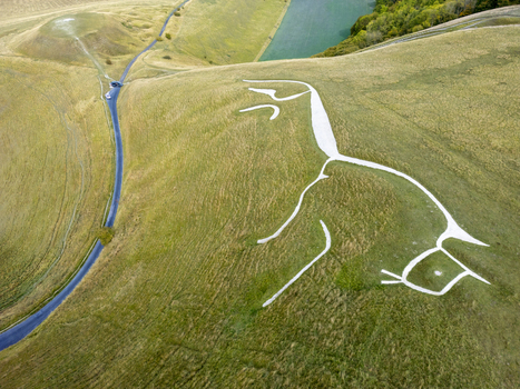 Aerial view of the Uffington White Horse a prehistoric hill figure carved into the chalk hillside surrounded by green rolling hills and a winding road in Faringdon England United Kingdom. Aerial view of the Uffington White Horse a prehistoric hill figure carved into the chalk hillside surrounded by green rolling hills and a winding road in Faringdon England United Kingdom.